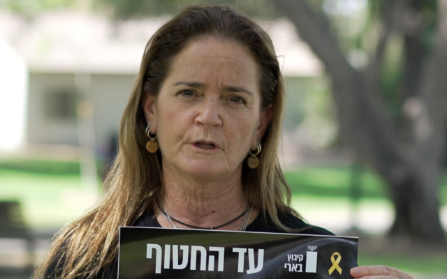 Nira Sharabi, veuve de l'otage assassiné Yossi Sharabi, tenant une affiche de son mari dans une vidéo du kibboutz Beeri réalisée à l'occasion du deuxième anniversaire de l'invasion et du massacre perpétrés par le Hamas. (Crédit : Autorisation)